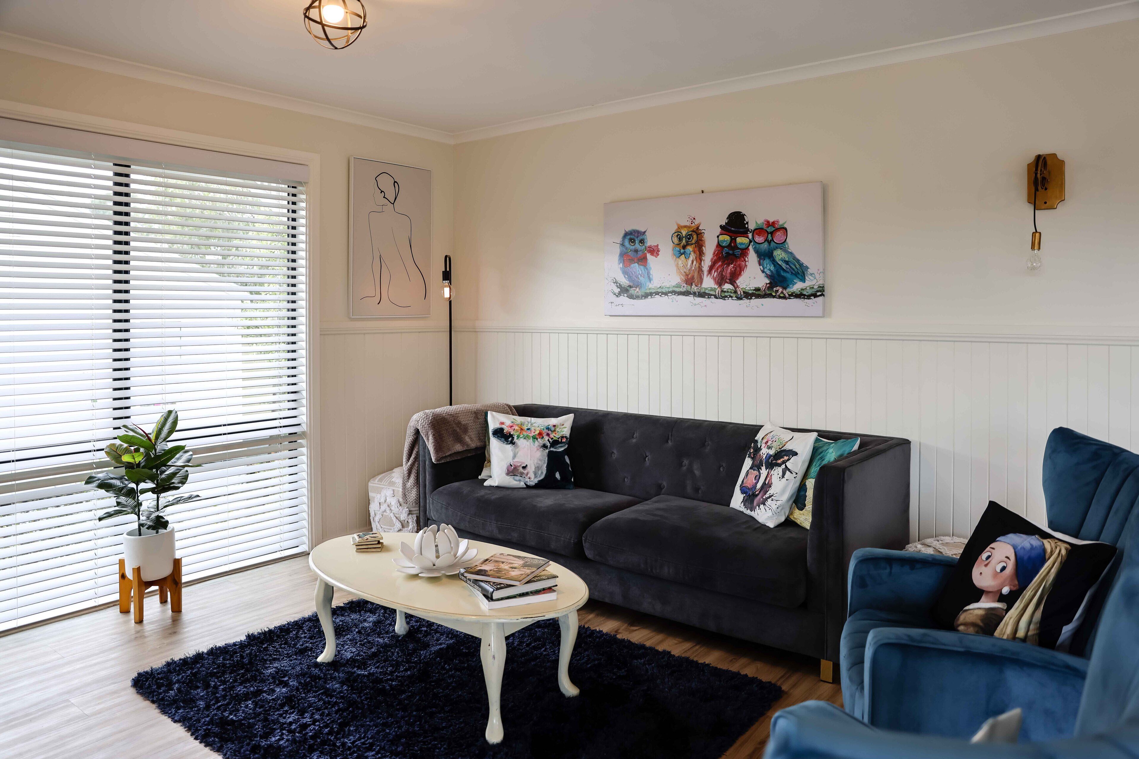 A living room with a dark blue sofa, a blue armchair, a white coffee table, and a potted plant.
