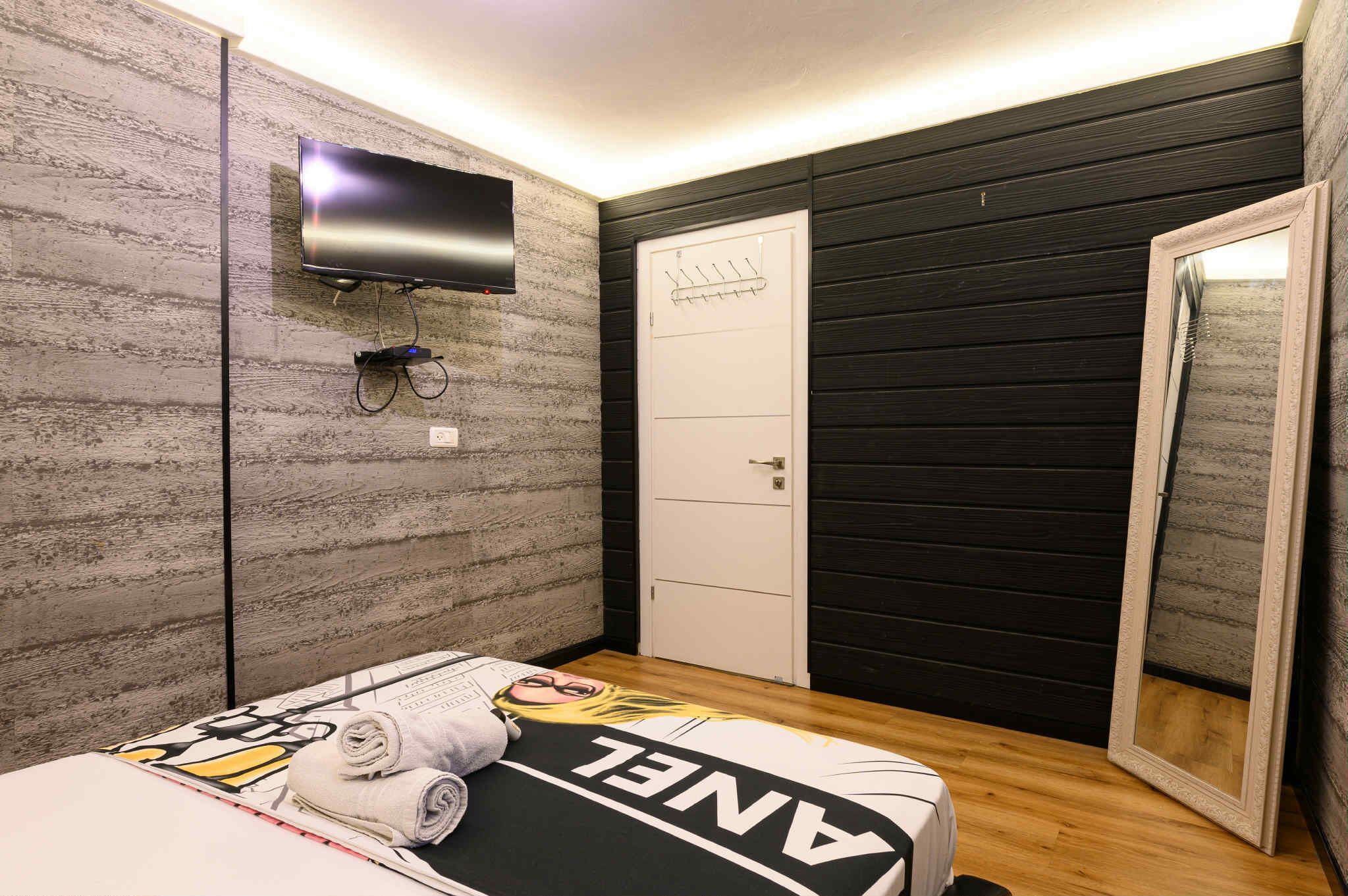 A bedroom with a bed, a TV mounted on the wall, a wardrobe, and a door.