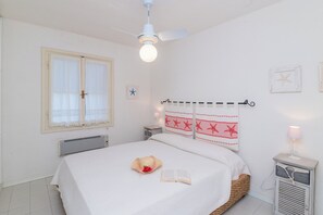 A bedroom with a bed, a ceiling fan, a radiator, a bedside table with a lamp, and a window with curtains.