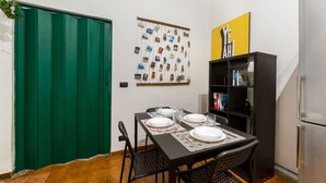 Un coin repas avec une table dressée pour quatre personnes, une porte verte, un collage de photos accroché au mur et une bibliothèque noire.