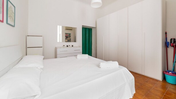 Une chambre à coucher avec un lit, une commode, un miroir, une porte verte et un balai.