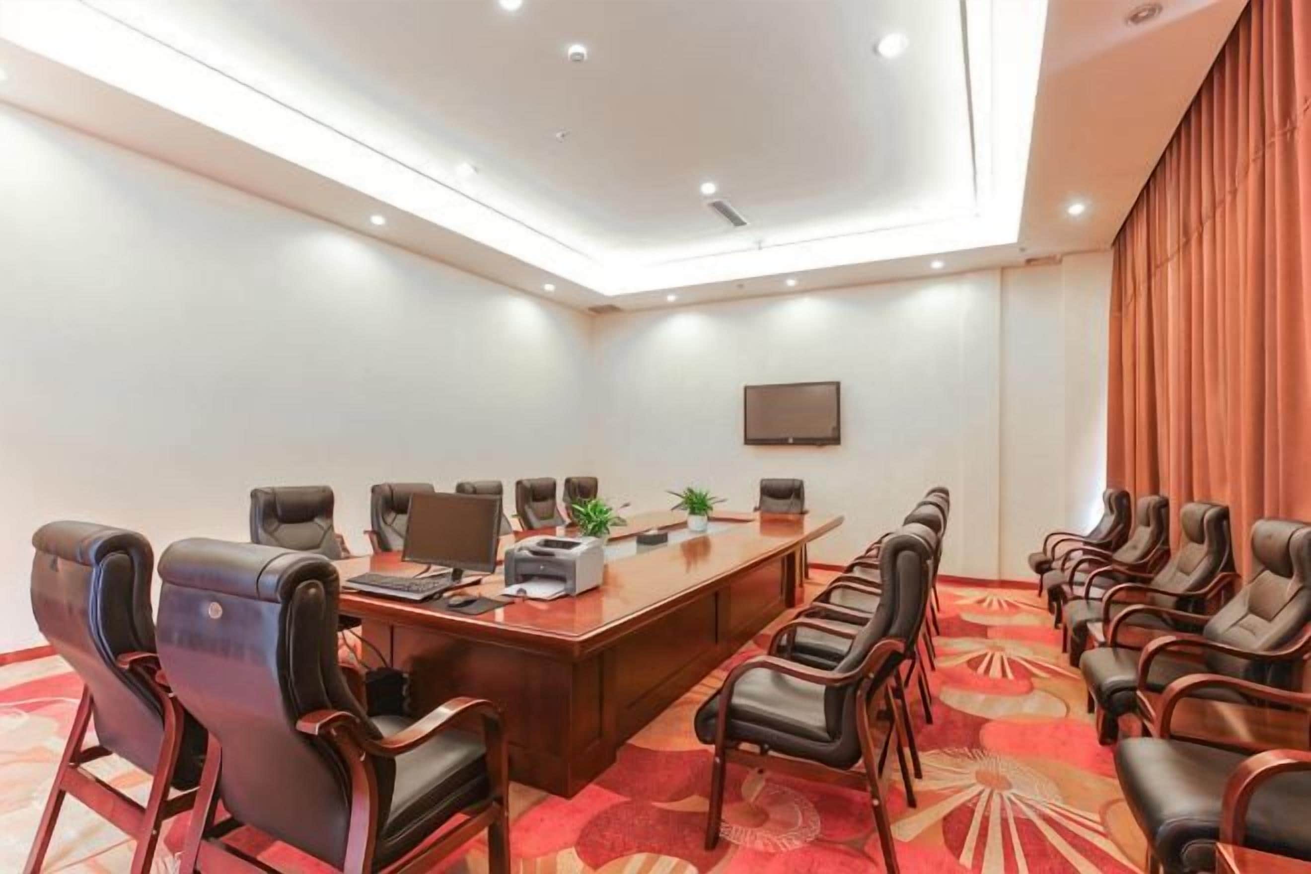 A conference room with a long table, multiple chairs, a plant, and a flat-screen TV on the wall.