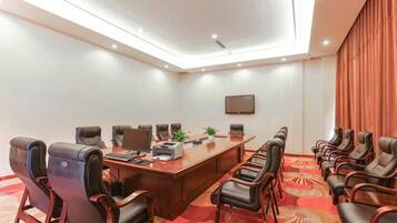 A conference room with a long table, multiple chairs, a plant, and a flat-screen TV on the wall.