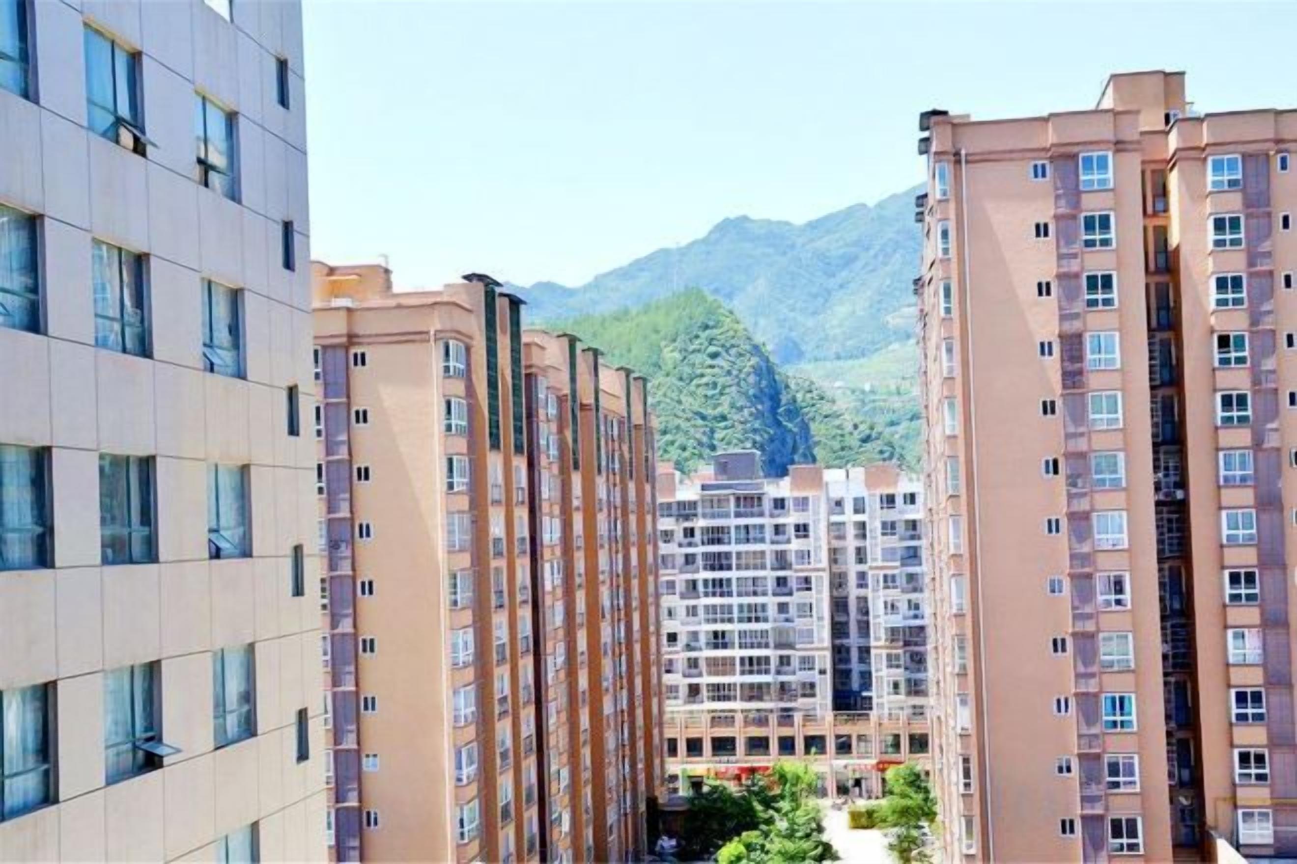 A multi-story residential building with balconies, a central courtyard, and a mountainous backdrop.