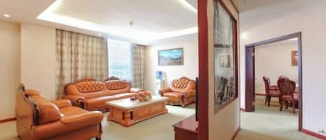 Quarto de hotel com sofá, mesa de centro, uma pintura e área de refeições com cadeiras e mesa.