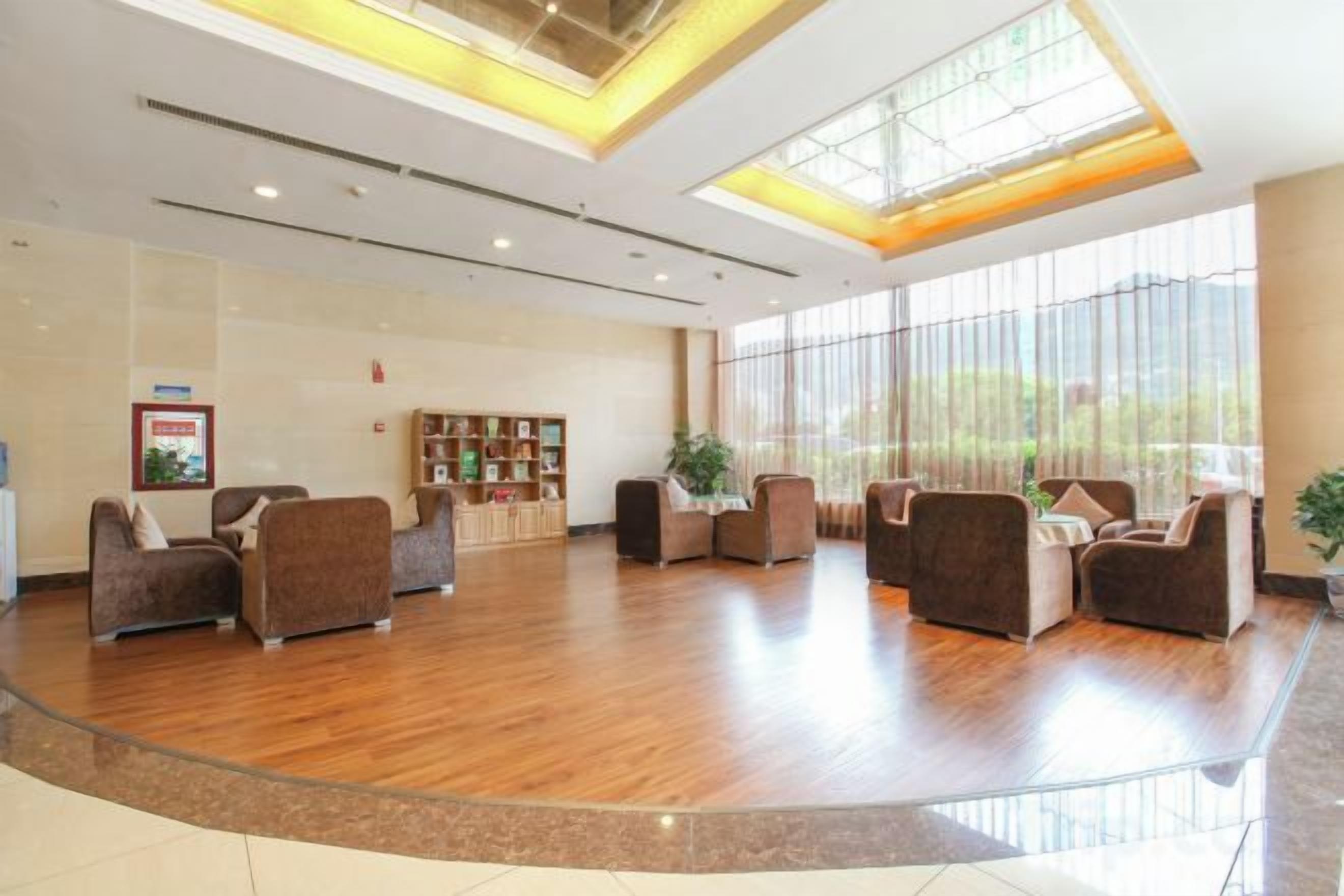 A spacious lobby with a curved glass partition, seating area with sofas, a reception desk, and a bookshelf.