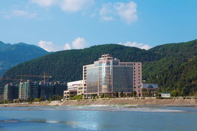 Un hotel de diseño moderno, situado cerca de una masa de agua con montañas al fondo.