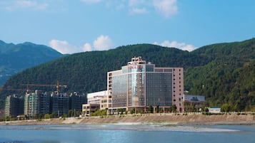 A hotel with a modern design, located near a body of water with mountains in the background.