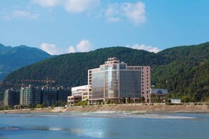 A hotel with a modern design, located near a body of water with mountains in the background. - Chao Tian Hotel (Guangyuan)
