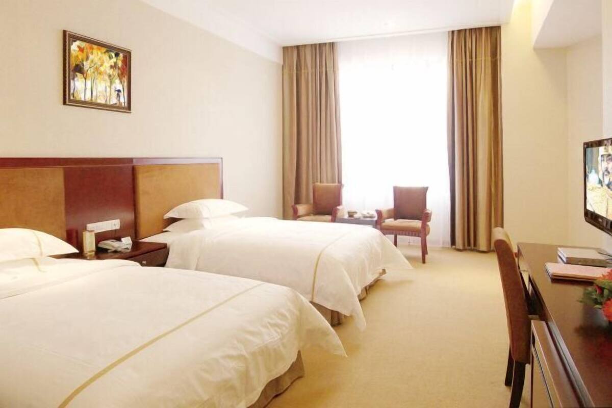Quarto de hotel com duas camas, uma mesa, uma cadeira e uma televisão.