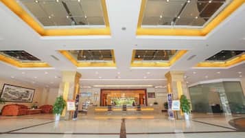 A spacious lobby with a central reception area, large windows, and a modern ceiling design.