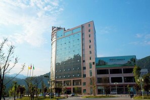 A multi-story building with a glass facade, a parking lot, and a smaller adjacent building with signage. - Chao Tian Hotel (Guangyuan)