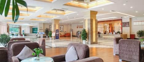 A hotel lobby with seating areas, a reception desk, and a large open space.