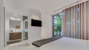 A modern bedroom with a large bed, a TV mounted on the wall, and a bathroom with a glass shower enclosure. - Green House - modern villa with a private rooftop pool in the south of Tenerife! (Guía de Isora)