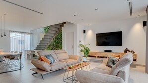 A modern living room with a sofa, coffee table, and TV. There is a staircase with greenery, a dining area, and a large window. - Green House - modern villa with a private rooftop pool in the south of Tenerife! (Guía de Isora)