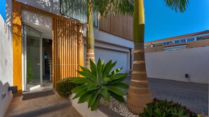 A modern building with a glass entrance, a wooden slatted wall, and a large agave plant in the foreground. - Green House - modern villa with a private rooftop pool in the south of Tenerife! (Guía de Isora)