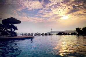 A pool with lounge chairs, a thatched umbrella, and a sunset view. - Huidong Biguiyuan Shiliyintan One Mile Sunshine Apartment (Huidong)