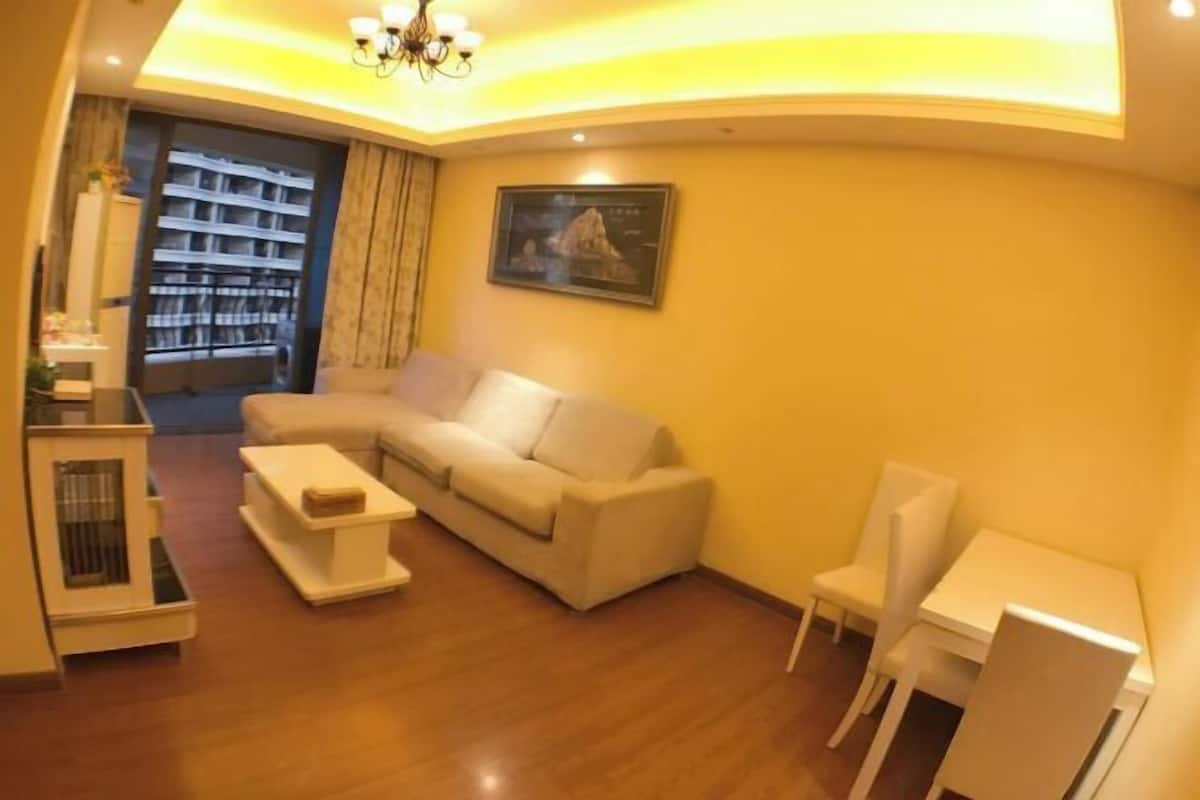 A living room with a sofa, a coffee table, a dining table with chairs, a bookshelf, and a framed picture on the wall.