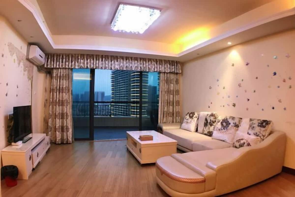 A living room with a sofa, a coffee table, a TV, and a balcony with a city view.