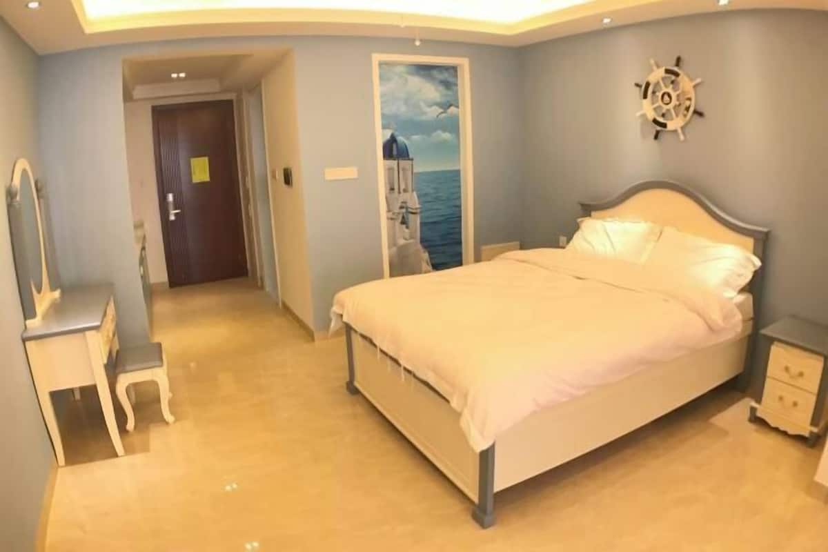 A bedroom with a bed, a nightstand, a dresser, and a door leading to another room.