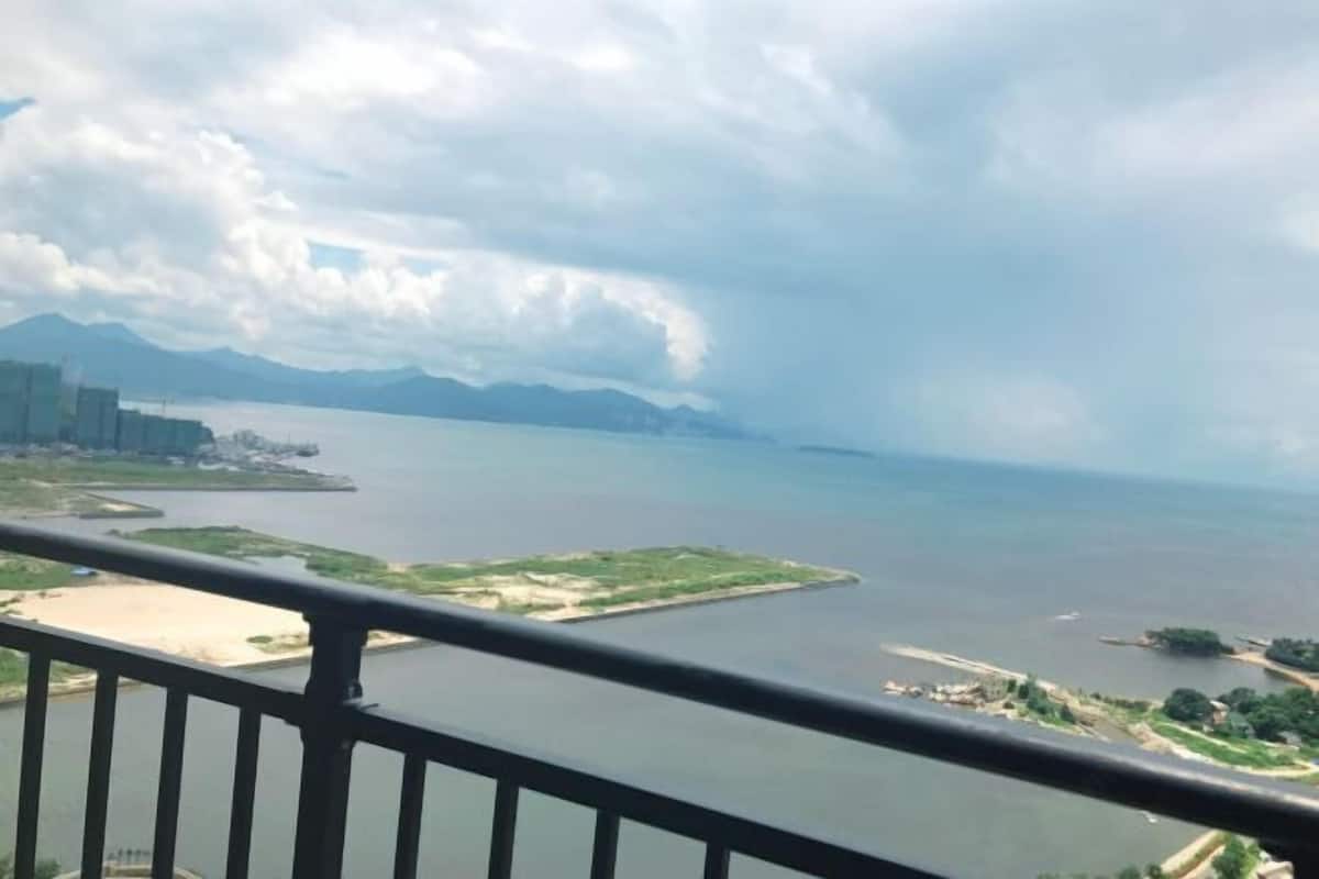 A coastal view from a balcony with a railing, a body of water, distant mountains, and a small island.