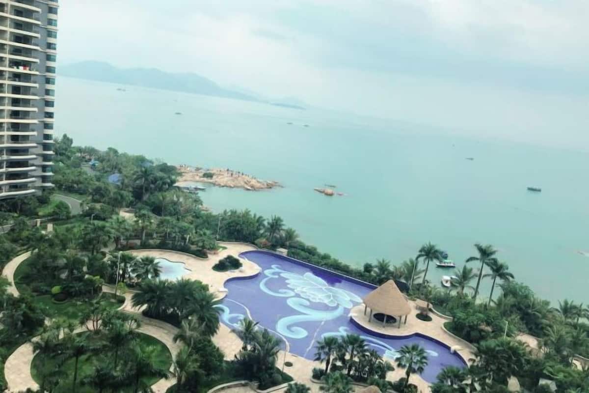 A resort with a large swimming pool, palm trees, and a view of the sea.