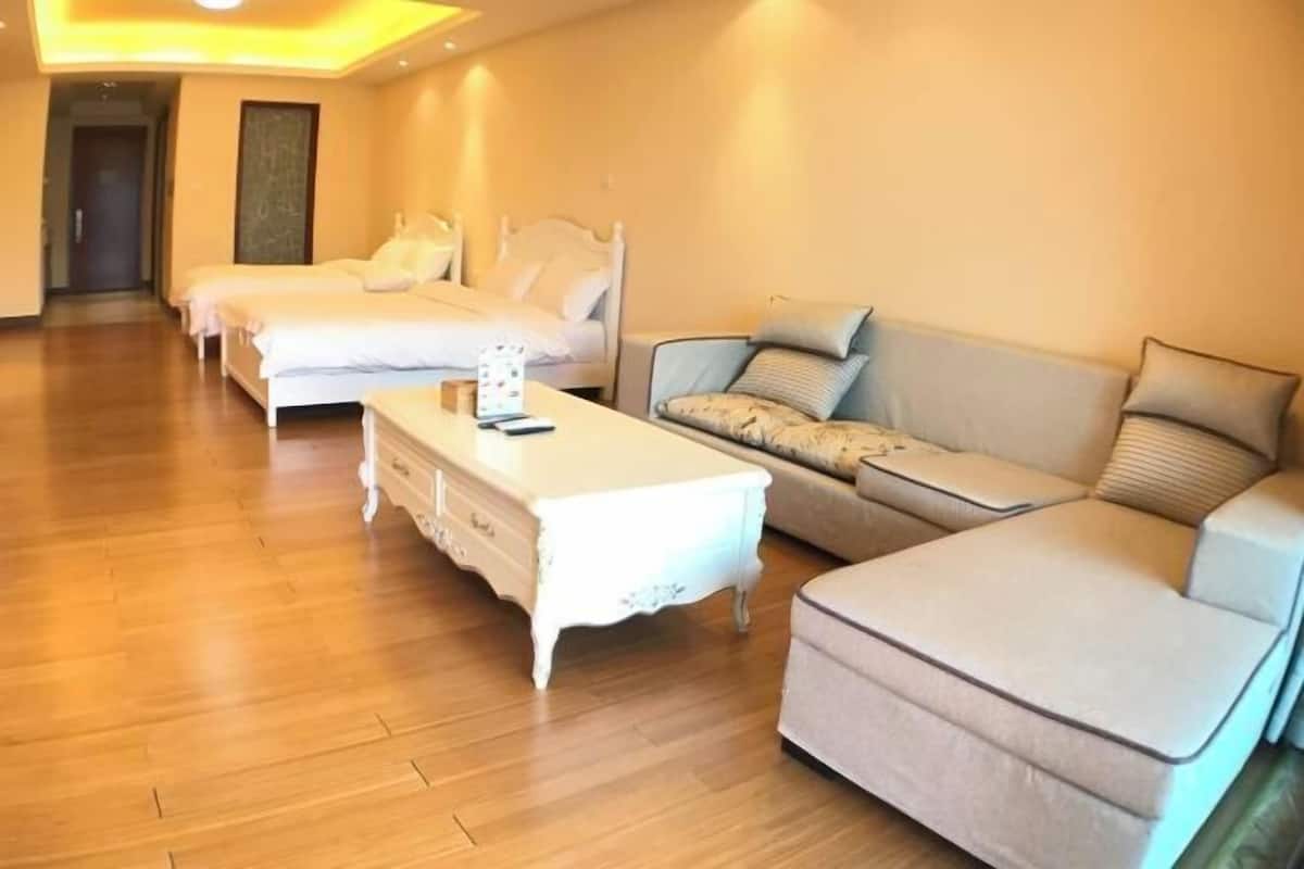 A hotel room with a wooden floor, two single beds, a sofa, and a white side table.