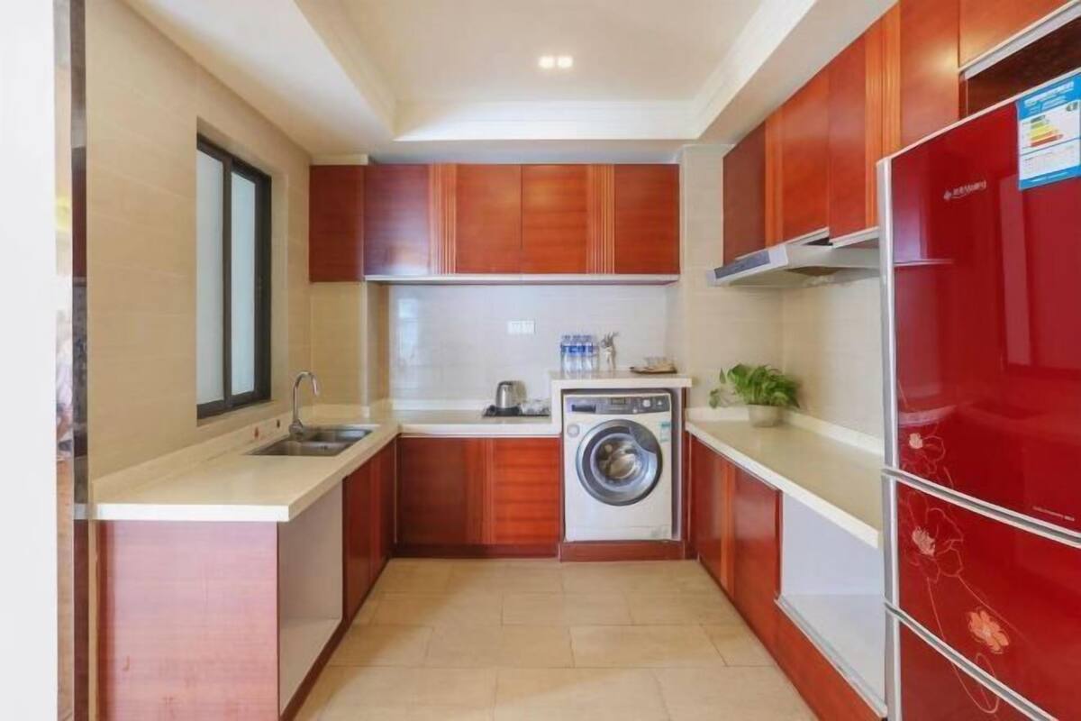 A compact kitchen with wooden cabinets, a washing machine, and a red refrigerator.
