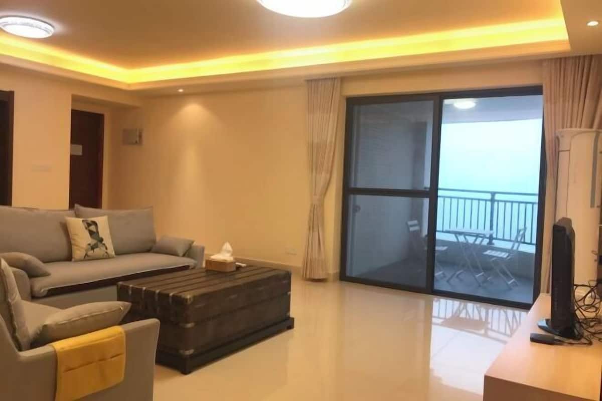 A living room with a sofa, a coffee table, a TV, and a sliding glass door leading to an outdoor area.