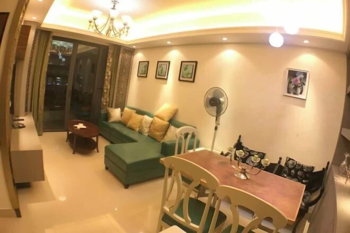 A living room with a green sofa, a dining table with chairs, a fan, and a chandelier.