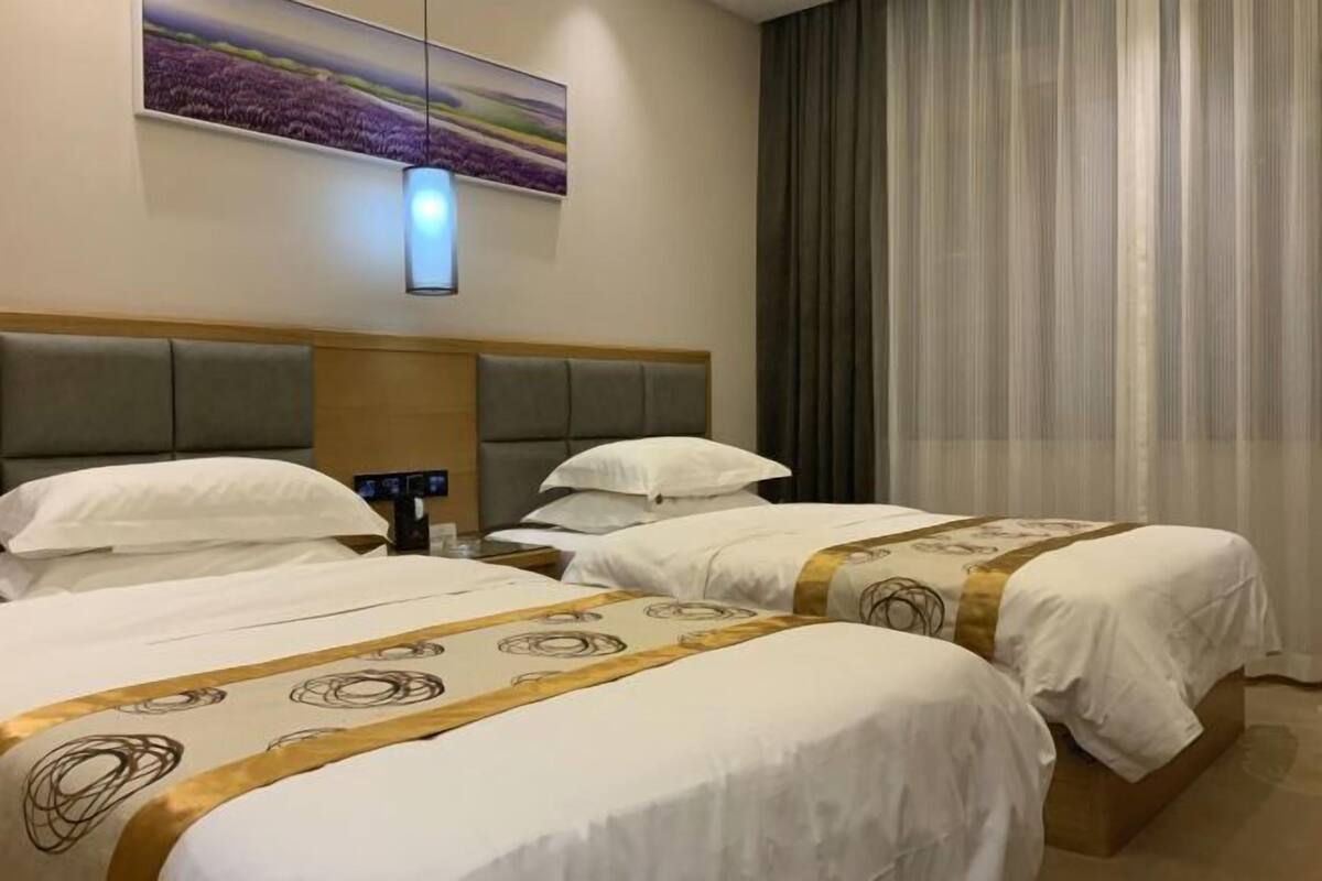 Habitación de hotel con dos camas, cabecera, mesita de noche, lámpara y un cuadro en la pared.