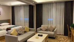 A hotel room with a bed, two sofas, a coffee table, and a dining table. - Jinjiaxiang Hotel (Xiji)