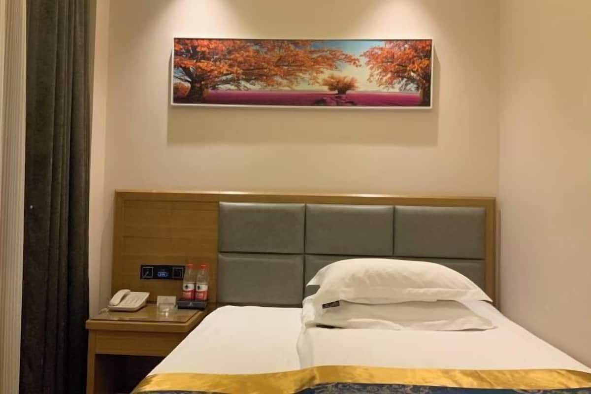 Una habitación de hotel con una cama, una mesita de noche con un teléfono y una botella, y un cuadro en la pared.