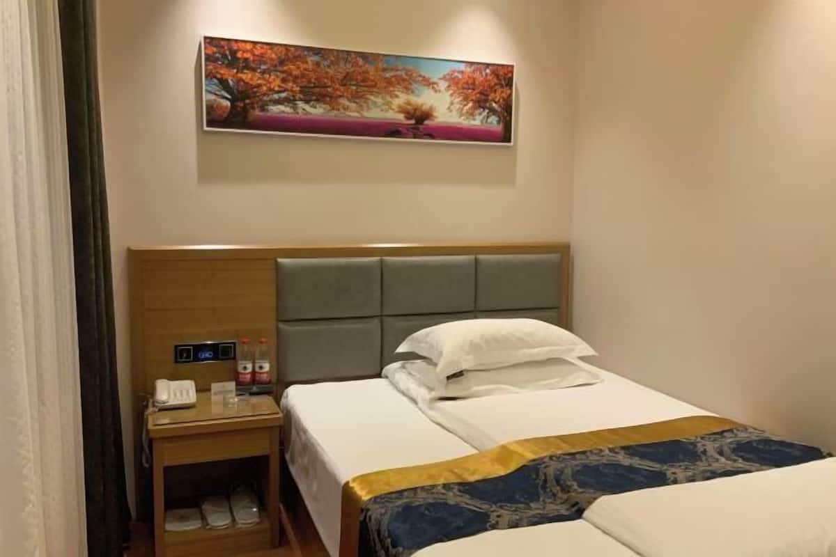 Habitación de hotel con cama, mesita de noche, un cuadro y una pequeña mesa con teléfono y botellas.