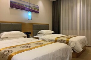A hotel room with two beds, a headboard, a bedside table, a lamp, and a painting on the wall.