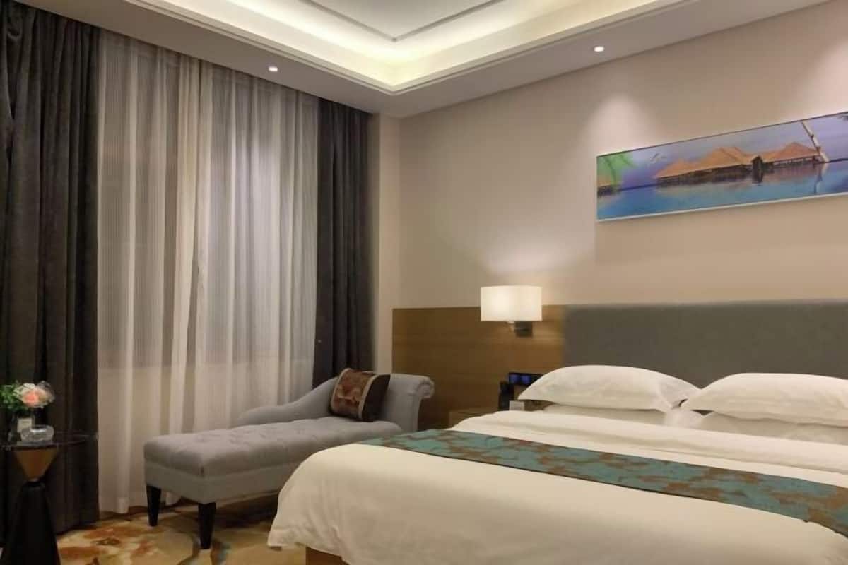 Una habitación de hotel con una cama grande, una silla, una mesita de noche, una lámpara y un cuadro en la pared.