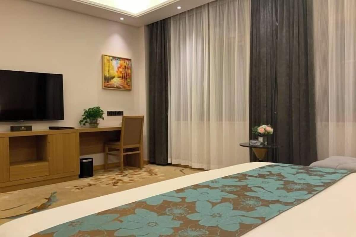 Una habitación de hotel con cama, escritorio, silla, televisor y un cuadro en la pared.