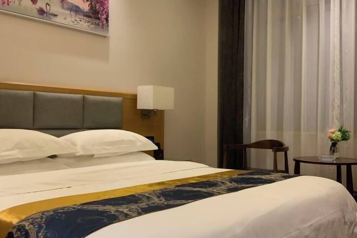 Habitación de hotel con una cama grande, una mesita de noche con lámpara, una silla y una pequeña mesa con un florero.