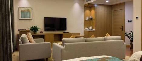 A hotel room with a bed, two sofas, a TV, and a desk with a plant.