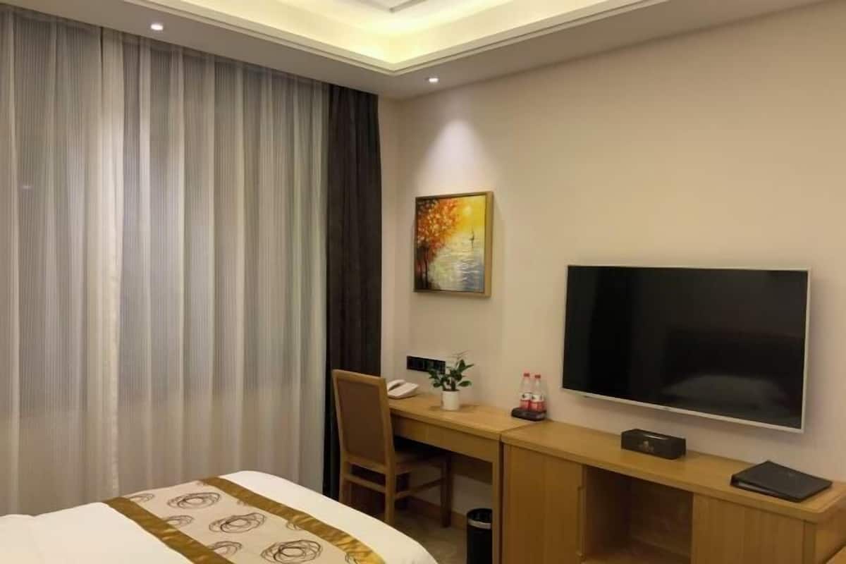 Habitación de hotel con cama, escritorio, silla, televisión y un cuadro en la pared.