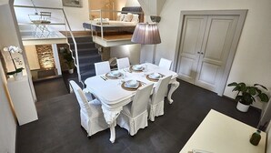 Een eethoek met een witte tafel gedekt voor vier personen, een trap naar een hoger niveau, en een deur aan de rechterkant.