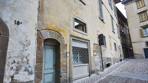 Een smalle straat met cobblestones, met een gebouw dat een stenen boog, een blauwe deur en een metalen hekwerk heeft.