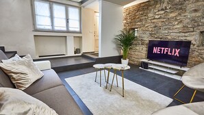 Een moderne woonkamer met een stenen muur, een groot televisiescherm, een bank, een salontafel en een potplant.