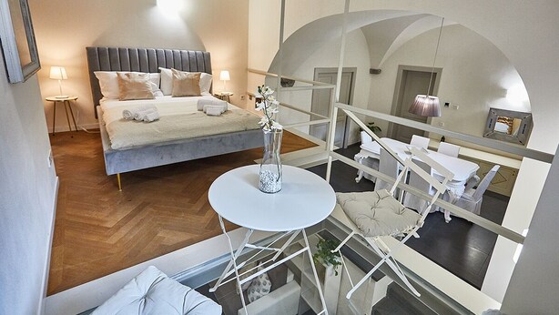 Een moderne hotelkamer met een groot bed, een ronde tafel met een vaas en een balkon met witte meubels.