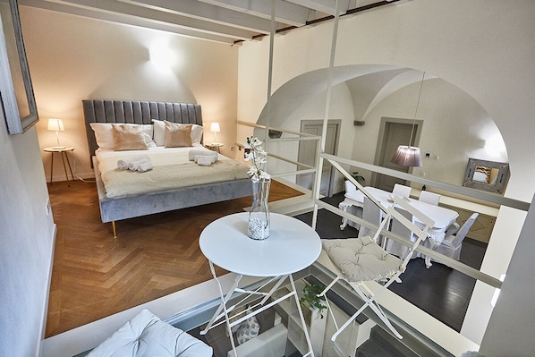 Une chambre d’hôtel moderne avec un grand lit, une table ronde ornée d’un vase et un balcon doté de mobilier blanc.