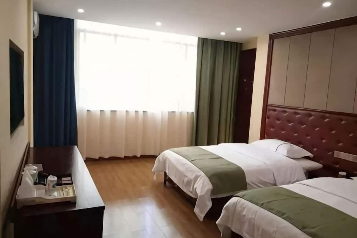 A hotel room with two beds, a wooden desk, a window with curtains, and a padded headboard.