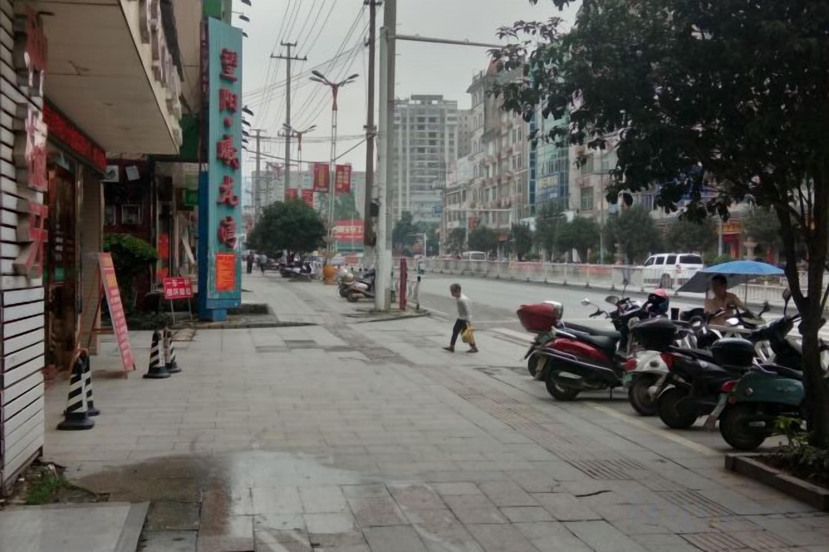 A street with shops, parked motorcycles, and a pedestrian.
