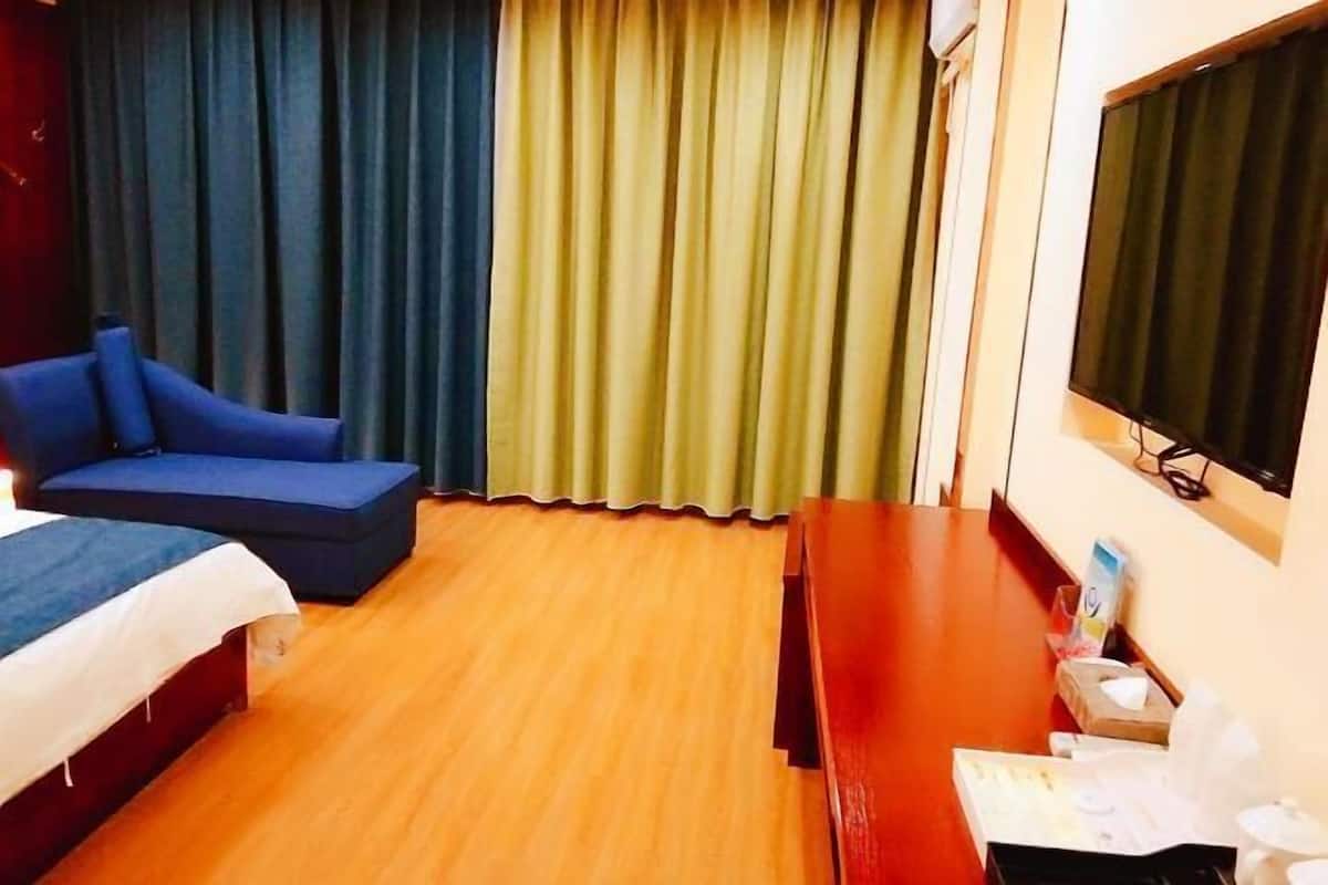A hotel room with a bed, a blue sofa, a wooden floor, a TV, and curtains.