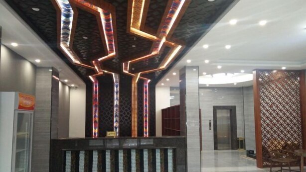 A modern reception area with a geometric light installation on the ceiling, a reception desk, and a seating area with a wooden partition. - Hengxi Boutique Hotel (Dahua)