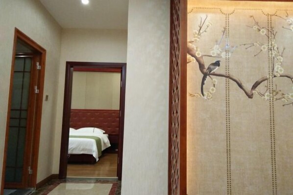 A hallway with a bed in the background, a wooden door, and a decorative wall with a tree and flowers. - Hengxi Boutique Hotel (Dahua)